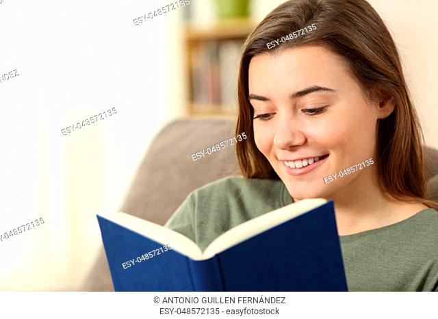 Teen reading a paper book sitting on a couch in the living room at home