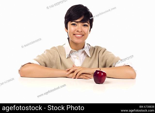 Smiling mixed-race young adult female sitting at white table with apple isolated on a white background