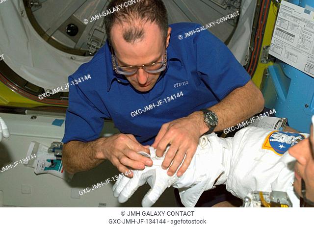 Astronaut Donald R. Pettit, NASA ISS science officer, assists astronaut John B. Herrington (partially out of frame), STS-113 mission specialist