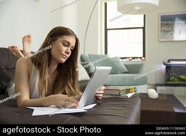 Woman using digital tablet to study on sofa