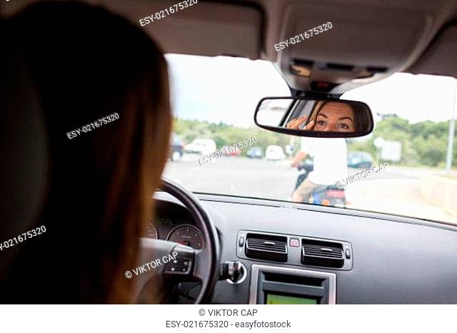 Young, woman driving a car, going home from work, fixing her make-up, checking herself in the rearview mirror