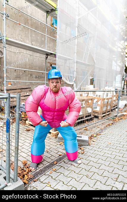 Portrait of man wearing pink bodybuilder costume and hard hat at construction site