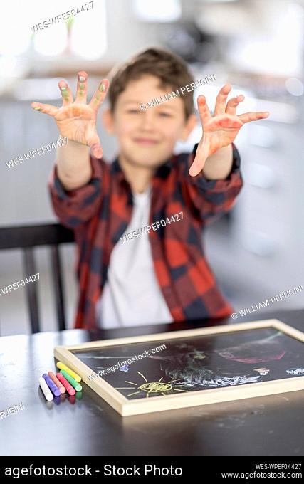 Boy showing dirty hands in front of slate at home