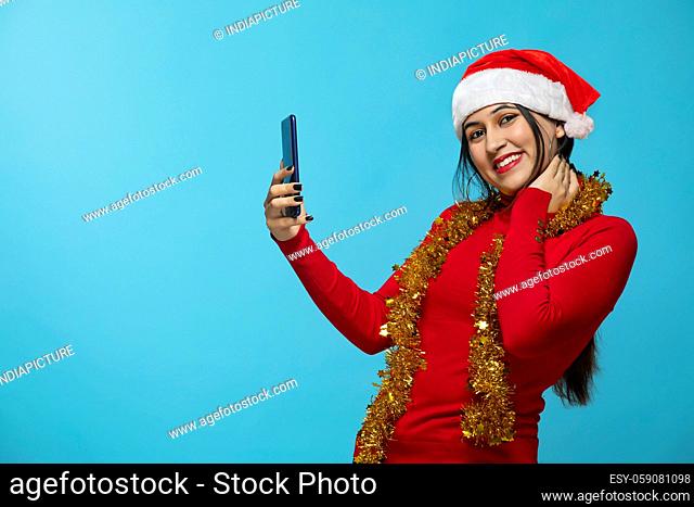 A portrait of a woman with Santa hat holding mobile phone