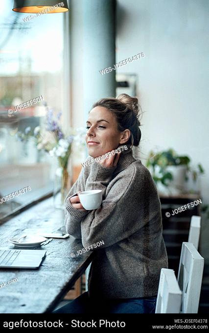 Thoughtful female entrepreneur with coffee cup by window at cafe