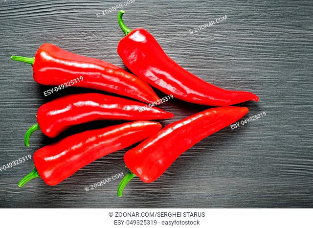 Five ripe sweet red Kapia peppers on dark shale stone background llying as arrow symbol