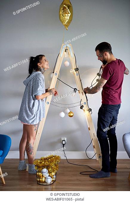Modern couple decorating the home at Christmas time using ladder as Christmas tree