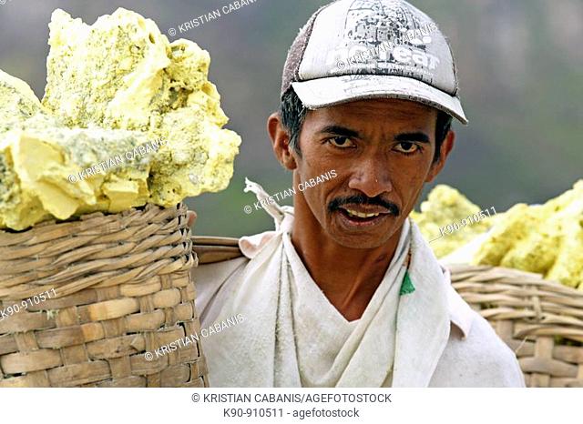 Portrait of worker carrying wicker baskets on his shoulder filled with yellow slices of sulphur, Kawah Ijen Volcano, East Java, Indonesia, Southeast Asia