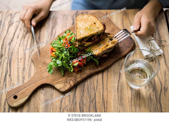 Hands holding knife and fork at wooden table with decorated salad and crusty bread