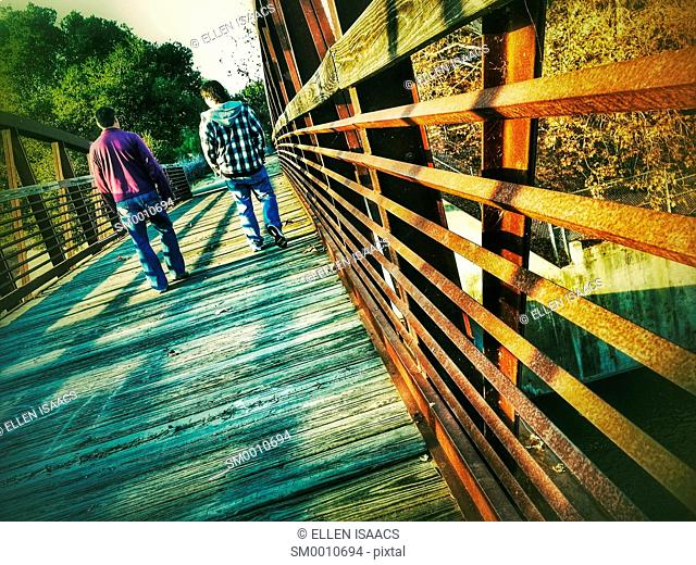 Two men walking casually into the distance across an iron bridge expressing a feeling of comfortable friendship