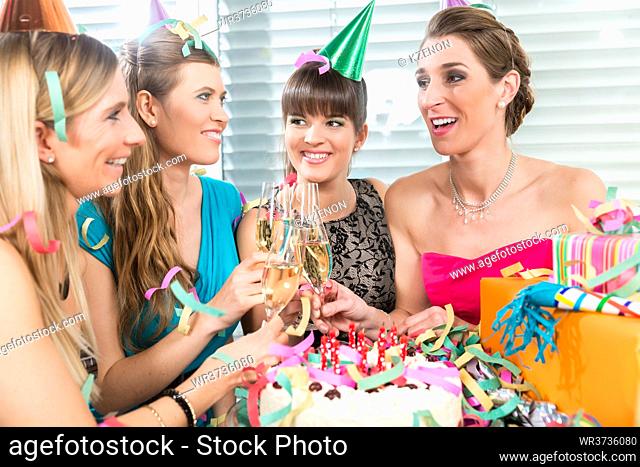 Four beautiful and cheerful women smiling while toasting with champagne during a surprise birthday party at home