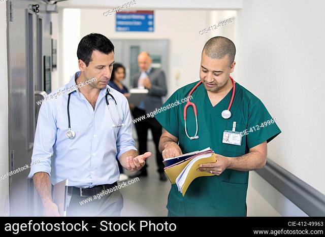 Male doctor and surgeon discussing medical chart, making rounds in hospital corridor