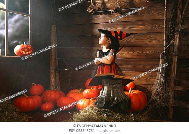 Halloween. little witch child conjures with book of spells, magic wand and pumpkins