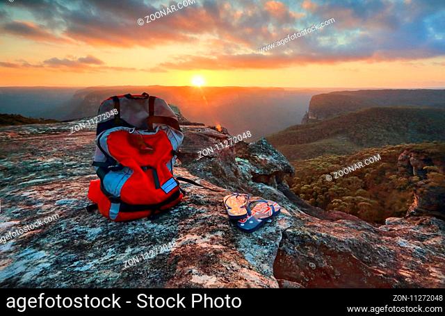 Sunset from a rocky outcrop of the Explorers Range, Blue Mountains Australia. A backpack and thongs with Australian flag sit catch the last light of the setting...