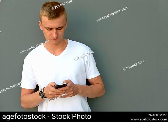 Portrait of young man with blond hair against gray concrete wall outdoors