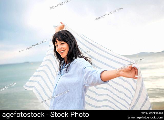 Smiling woman holding scarf near sea