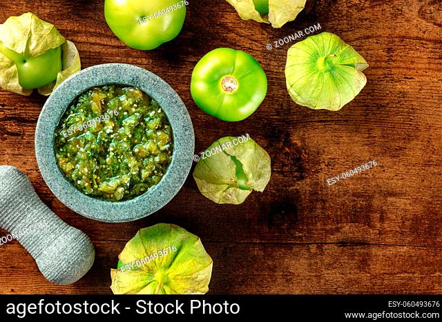 Tomatillos, green tomatoes, with salsa verde, green sauce, in a molcajete, traditional Mexican mortar, overhead flat lay shot with a place for text