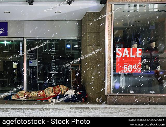 09 February 2021, Hamburg: A homeless person sleeps in the early morning in the entrance of a department store in the city centre