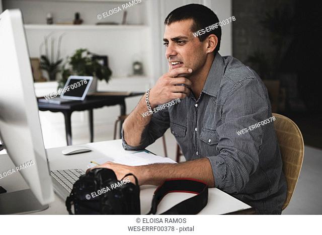 Young man with camera sitting at desk using computer
