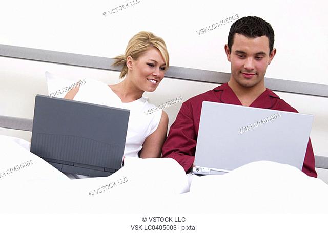 Couple in bed working on laptop computers