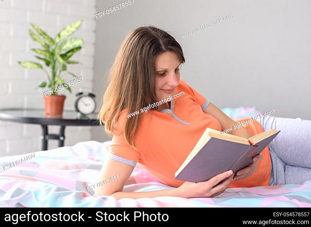 Girl at home lying in bed reads a book