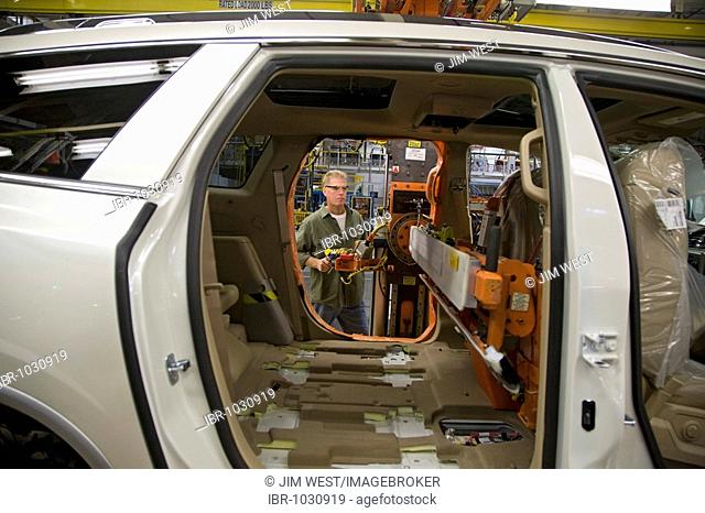 A worker using lifting equipment to slide seats into a car being assembled at a General Motors assembly plant which produces Buick, Saturn, and GMC vehicles