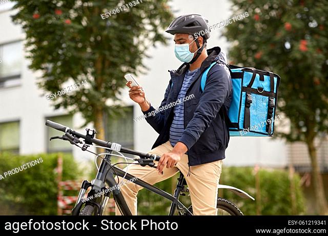 delivery man in mask with smatphone riding bicycle