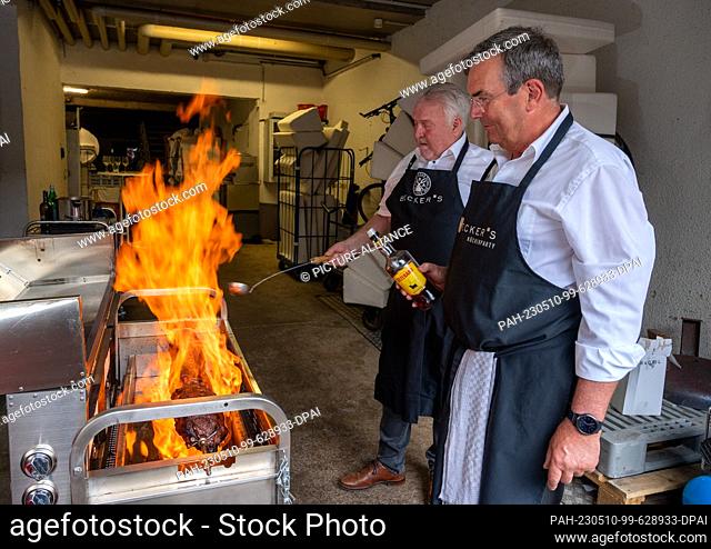 PRODUCTION - 08 May 2023, Rhineland-Palatinate, Trier: Arno Milde (front) and Reiner Honecker from the Spiessbratenclub Trier flambé the roast beef spit roast...