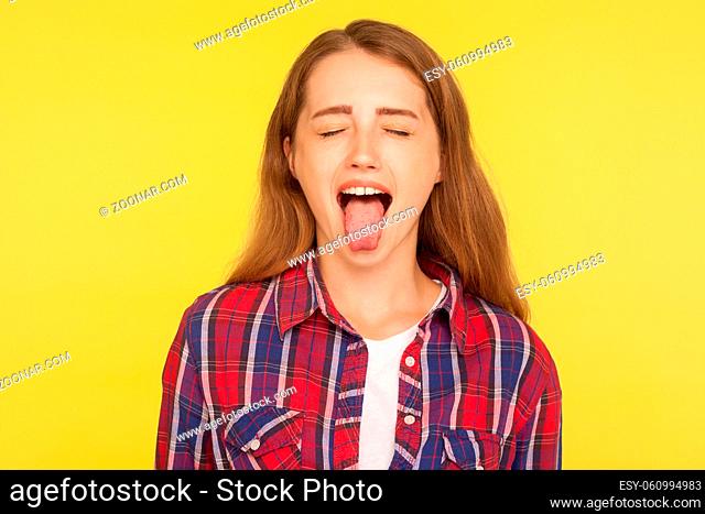 Portrait of naughty disobedient ginger girl in casual shirt standing with closed eyes and sticking out tongue, looking funny childish with derisive grimace