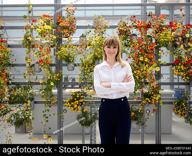 Smiling businesswoman with arms crossed standing against flowers in greenhouse