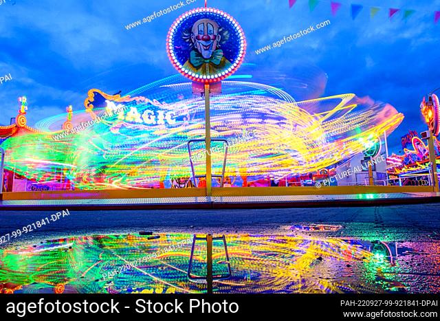 27 September 2022, Saxony-Anhalt, Magdeburg: A carousel turns in the evening at the autumn fair of the capital of Saxony-Anhalt, reflected in a puddle of rain