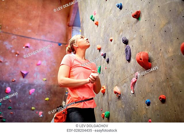 fitness, extreme sport, bouldering, people and healthy lifestyle concept - young woman with chalk bag exercising at indoor climbing gym wall