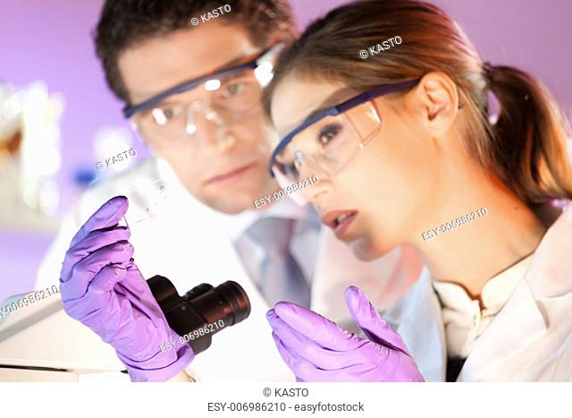 Attractive young scientist and her post doctoral supervisor looking at the microscope slide in the forensic laboratory
