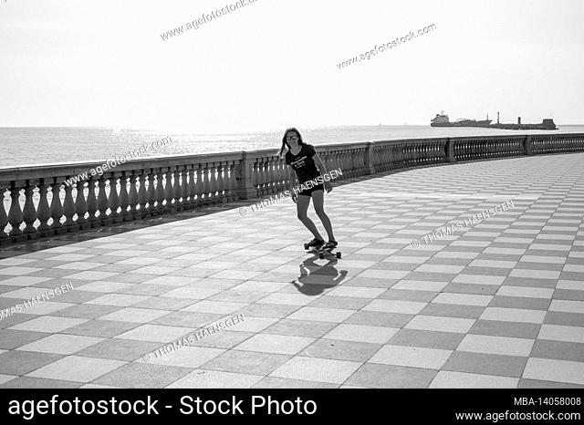 skater girl skating and jumping on terrazza mascagni in livorno, italy. its a wide sinuous belvedere toward the sea with a paving surface of 8700 sqm like a...