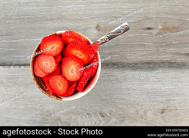 Table top view on small bowl of raspberries cut in small pieces, with silver spoon - ready to eat healthy snack