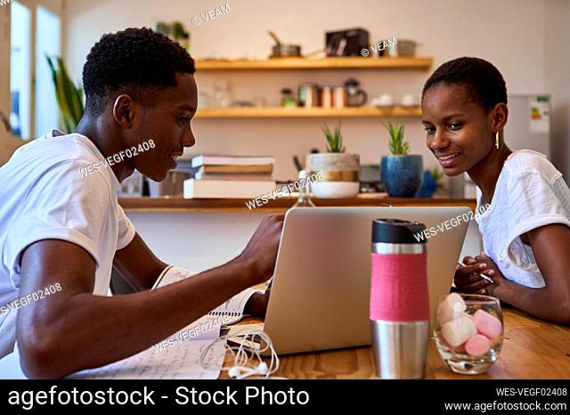 Smiling couple discussing doubts over laptop while studying at home