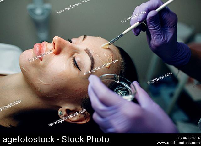Beautician applying with brush contact cold hydrogenation gel on face of woman for hardware procedures in beauty spa
