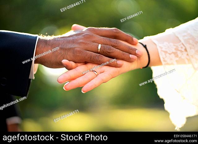 The hands of the bride and groom with the rings close up. A pair of hands of a dark-skinned groom and white bride with rings gently touch each other