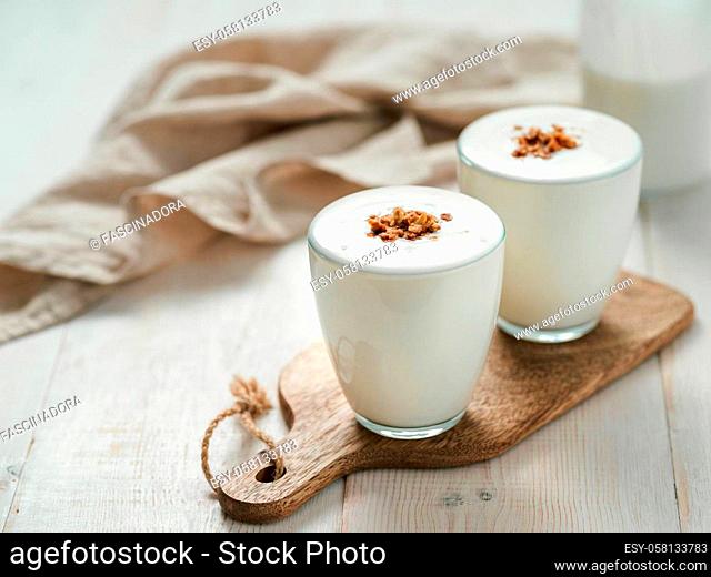 Kefir, buttermilk or yogurt with granola. Yogurt in glass on white wooden background. Probiotic cold fermented dairy drink