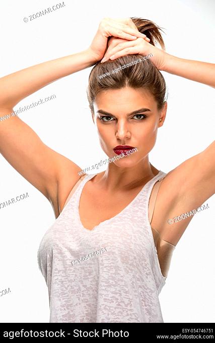 The dark-haired girl in a t-shirt. Hands holding hair in a bundle. Lips bright crimson color. In the studio on a white background. Vertical photo