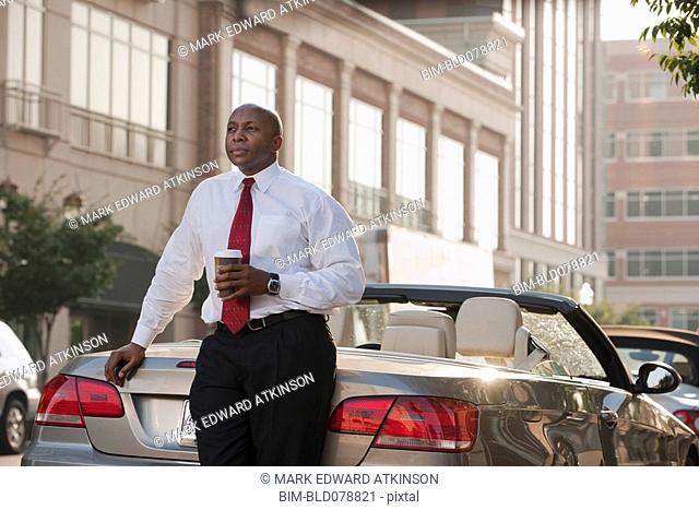Black businessman drinking coffee near convertible