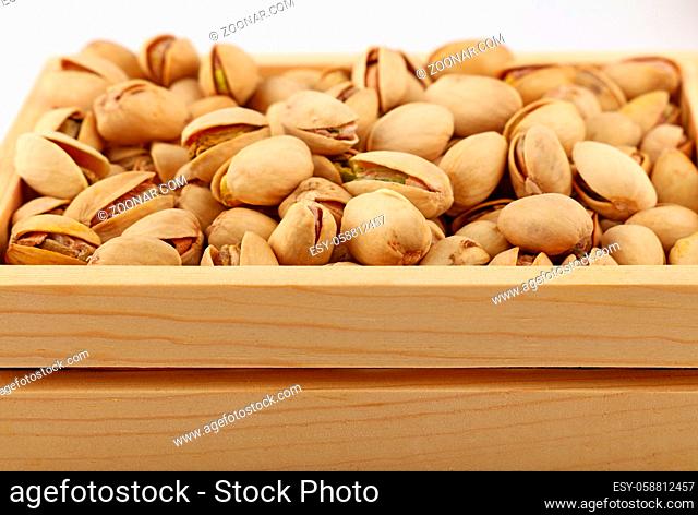 Close up fresh roasted pistachio nuts in wooden box over white background, low angle view