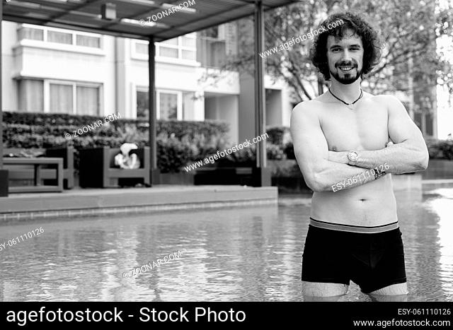 Portrait of handsome bearded man with curly hair shirtless relaxing beside the swimming pool in the city of Bangkok, Thailand