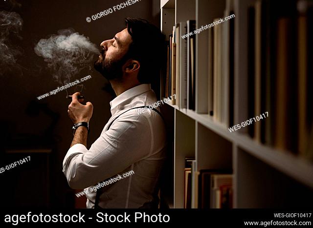 Portrait of bearded man smoking cigar in front of bookshelf