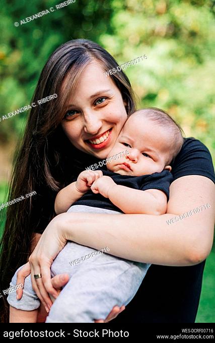 Smiling young woman carrying baby boy at park