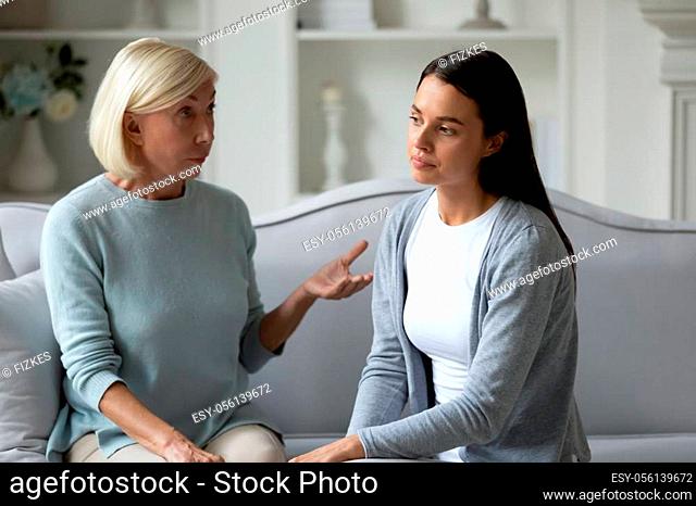 Serious middle age woman talking to stressed young daughter. Annoyed mature mother lecturing stubborn grown up child, sitting together on sofa