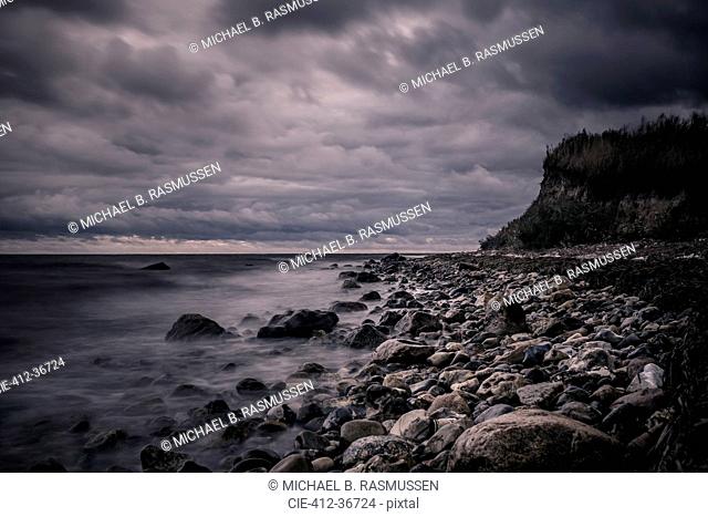 Tranquil rocks on ocean beach below stormy, overcast clouds, Bisserup, Denmark