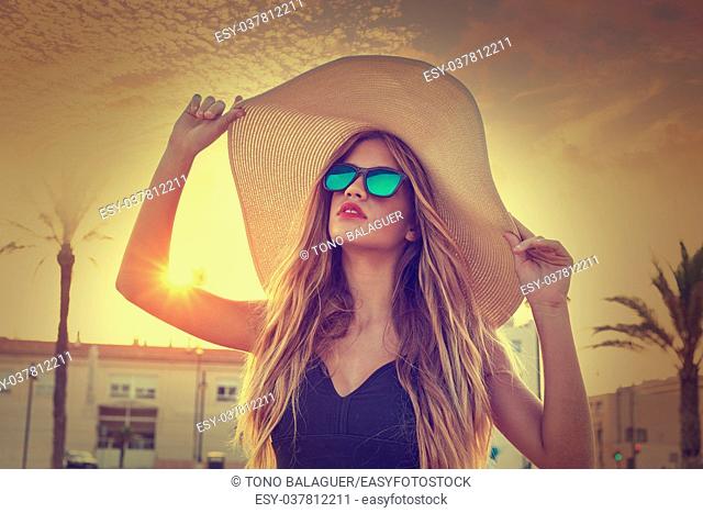 Blond teen girl sunglasses and pamela sun hat at palm tree sunset filtered image