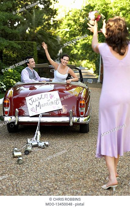 Bride and groom in vintage car bride throwing bouquet to woman