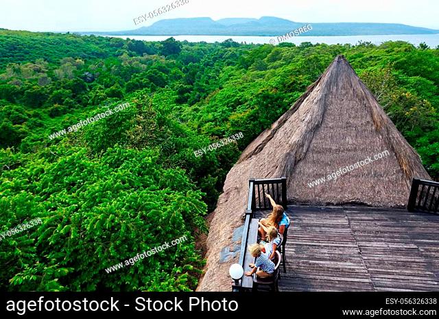 Happy family travel, explore Menjangan rainforest near Pemuteran. Mother, kids relax on lounge veranda with tropical jungle view